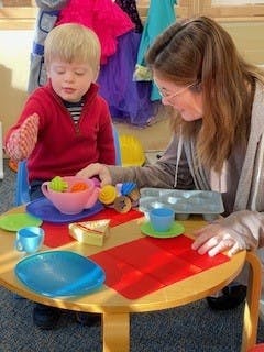 Adult and child playing with toy dishes at a small table