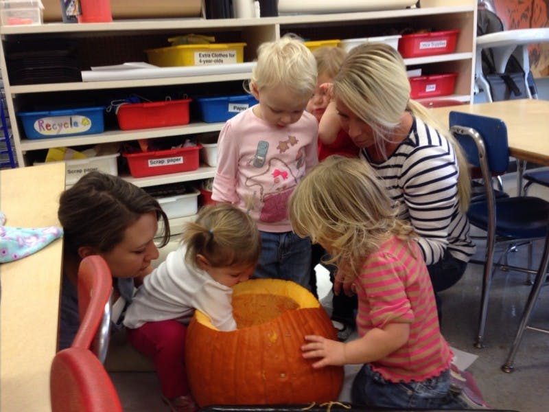 Two people and three children looking at a pumpkin in a classroom