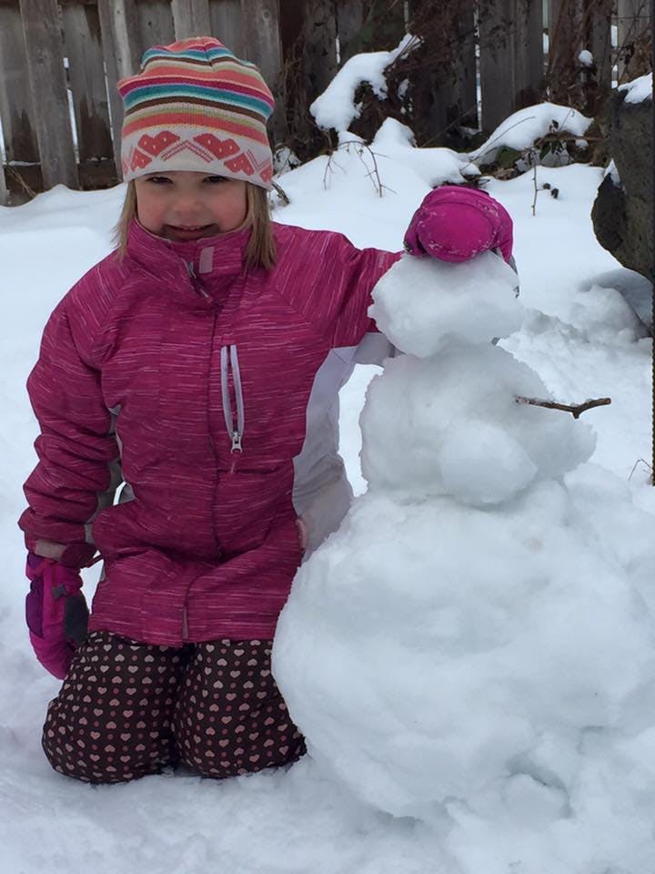 Child kneeling in snow next to a snowman