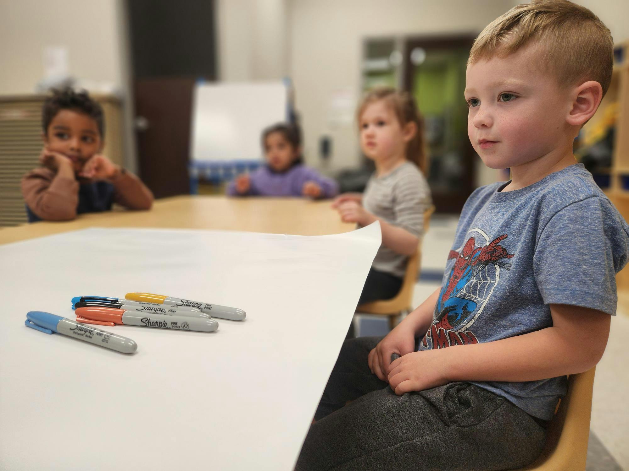 Children sitting at a table with markers and paper