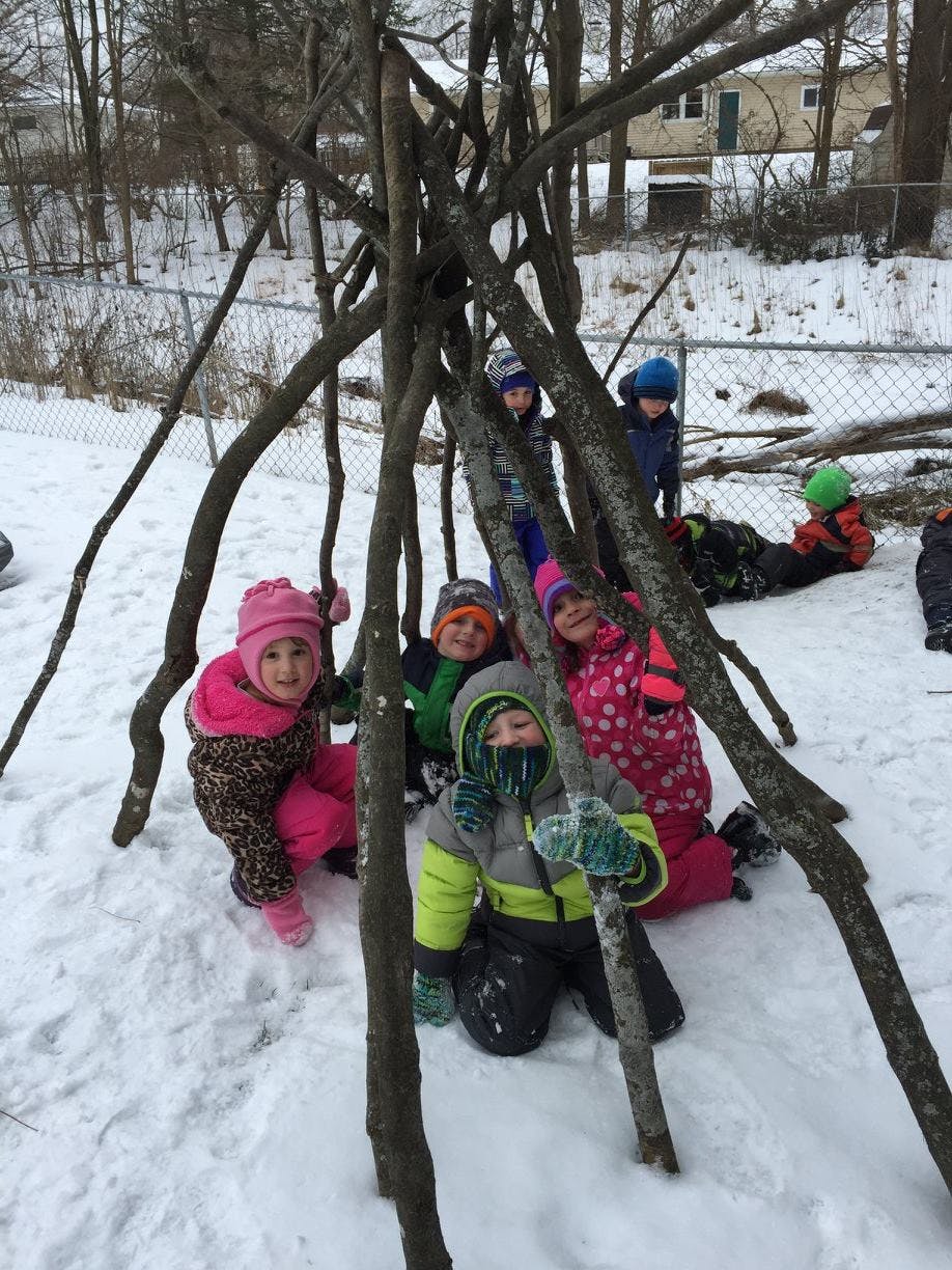 Children in winter clothing playing in a snow-covered area with branches