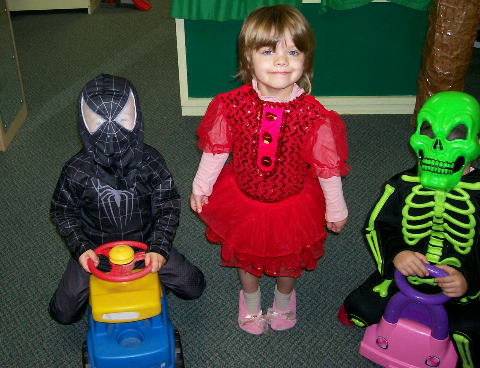 Three children in costumes, two on ride-on toys