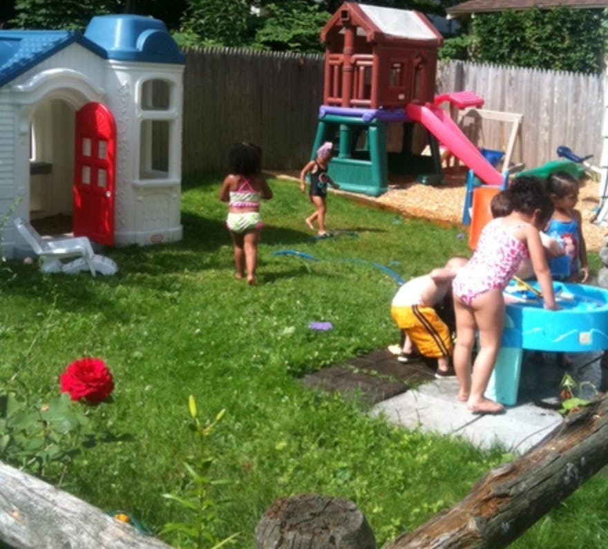 Children playing in a backyard with a playhouse and water table