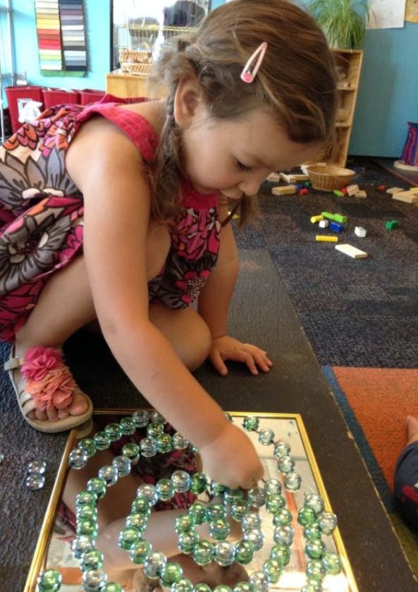 Child playing with glass beads on a mirror