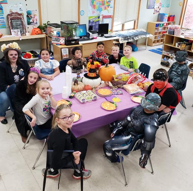 People and children in costumes sitting around a table with food
