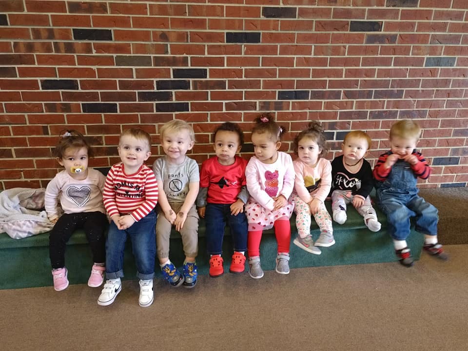 Group of young children sitting on a bench against a brick wall