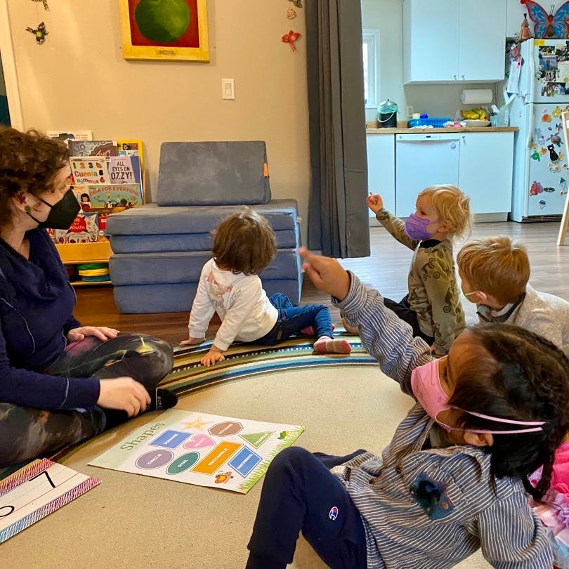 Adult and children sitting on floor in classroom, some wearing masks
