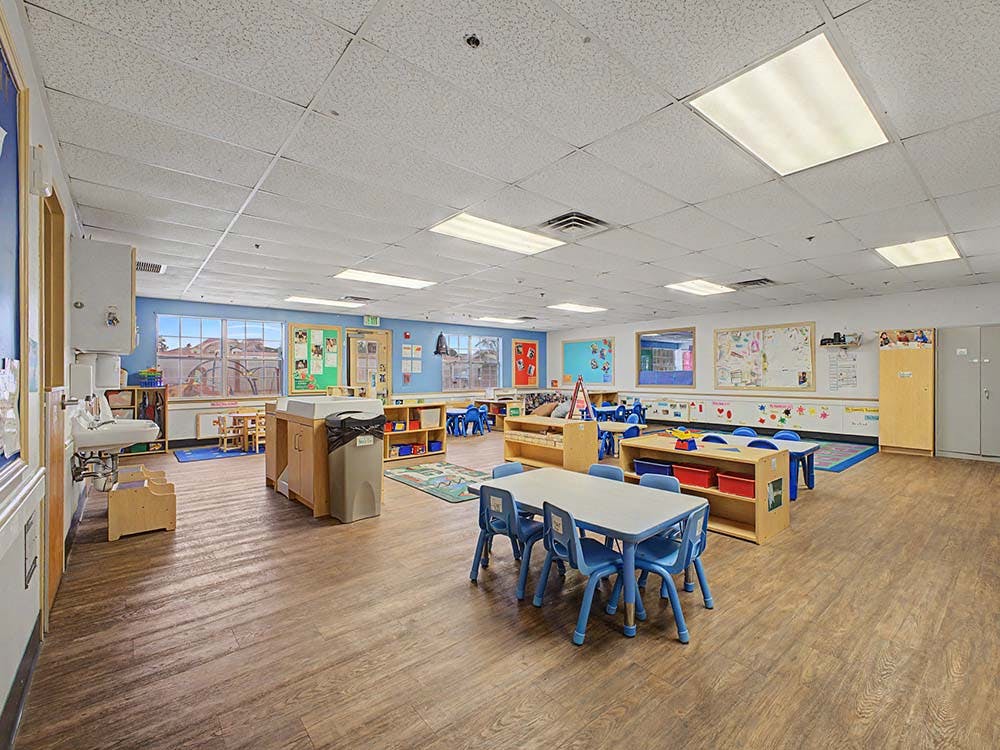 A colorful empty classroom with small tables, chairs, and learning materials