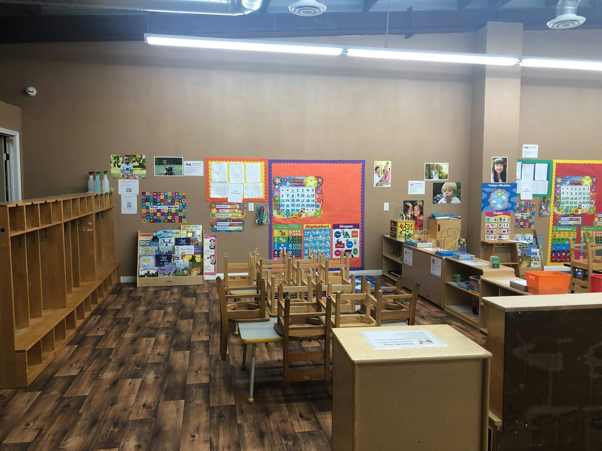 Empty classroom with small chairs and tables, cubbies, and colorful wall decorations