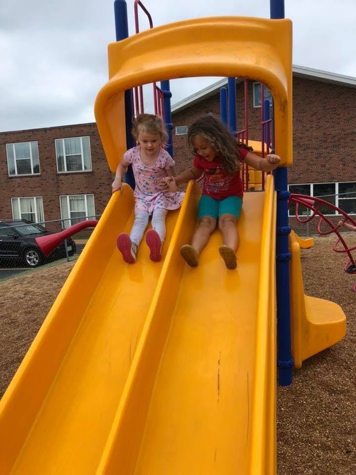 Two children going down a yellow slide on a playground