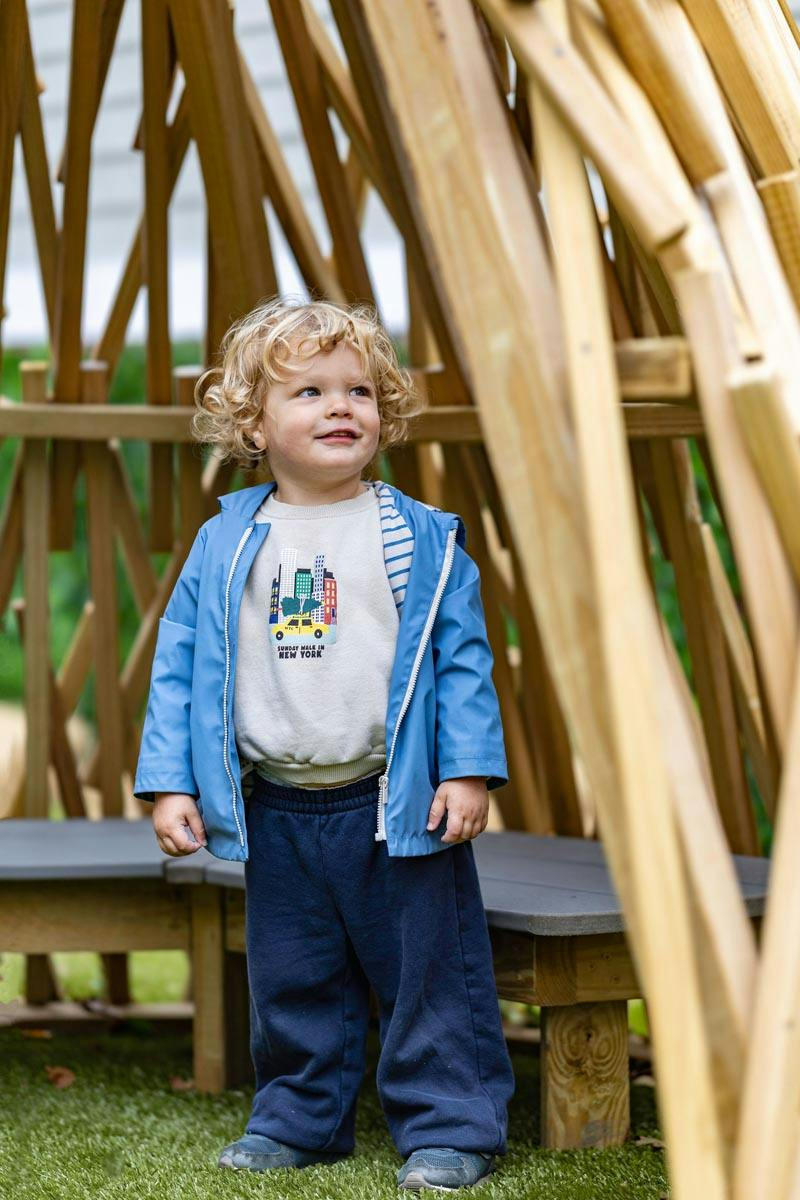 Child wearing a blue jacket standing inside a wooden play structure
