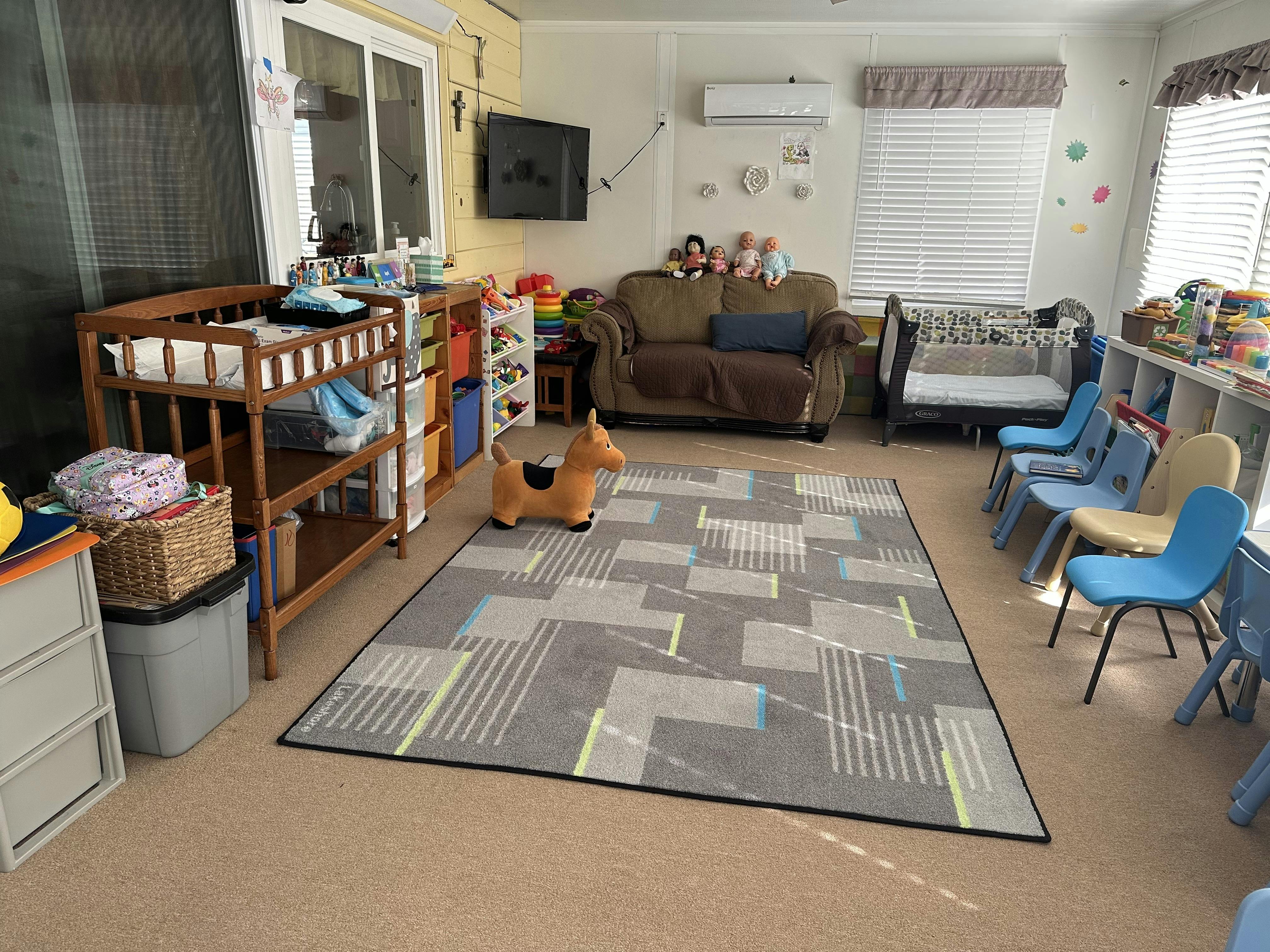 A room set up for children with a rug, small chairs, playpen, changing table, and toys