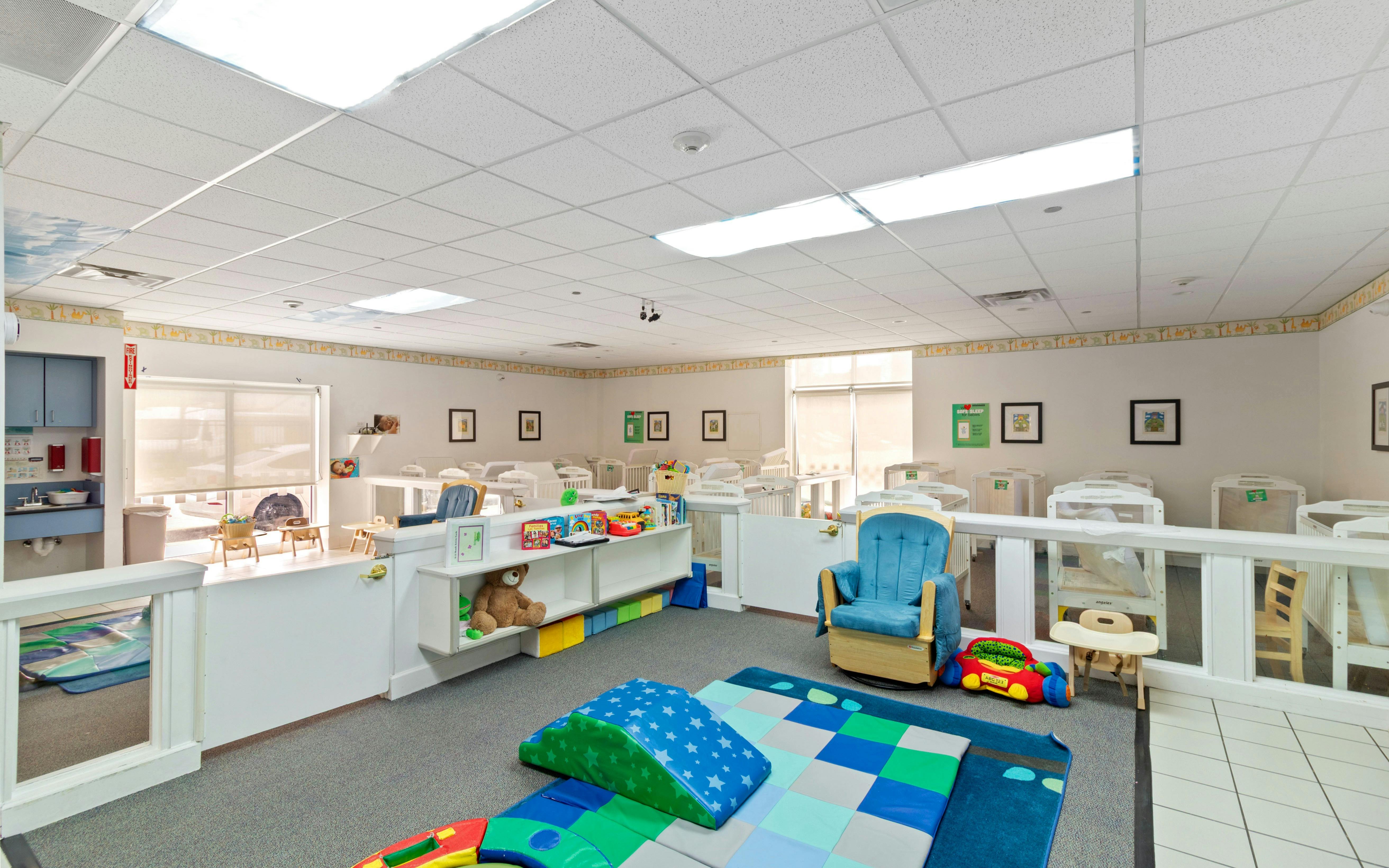 Daycare room with cribs, playmats, and a rocking chair