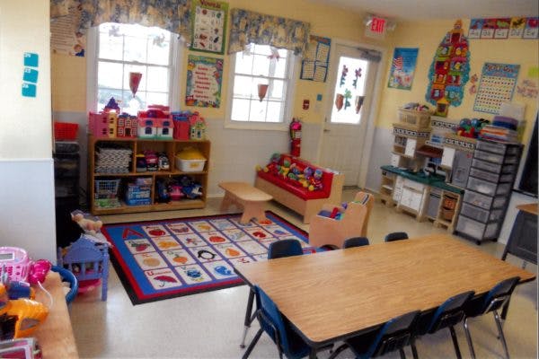 Classroom with a long table and chairs, play area with rug, and windows