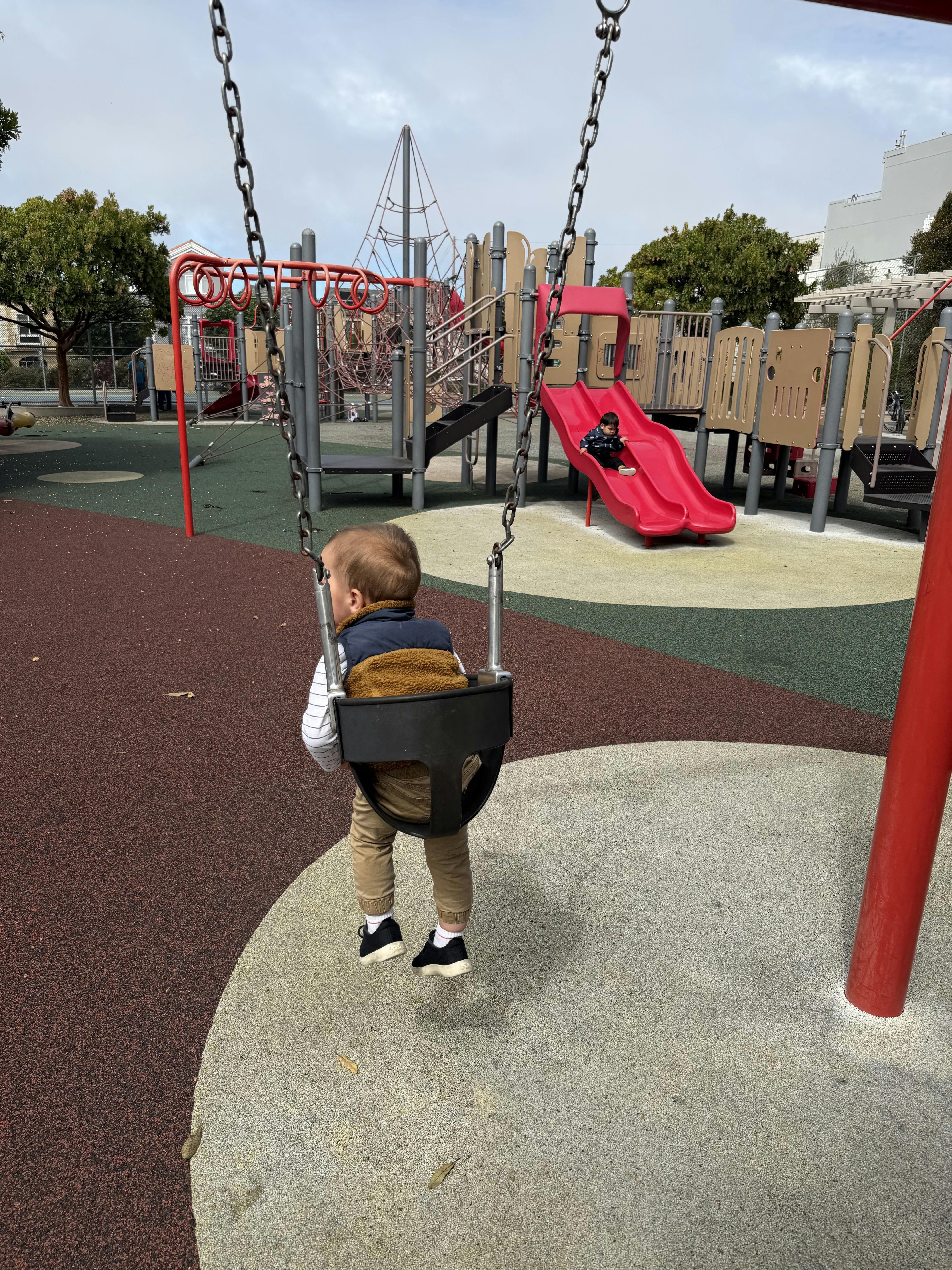 Child on a playground swing with another child on a nearby slide