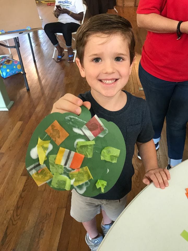 Child holding up a green paper craft with colorful squares
