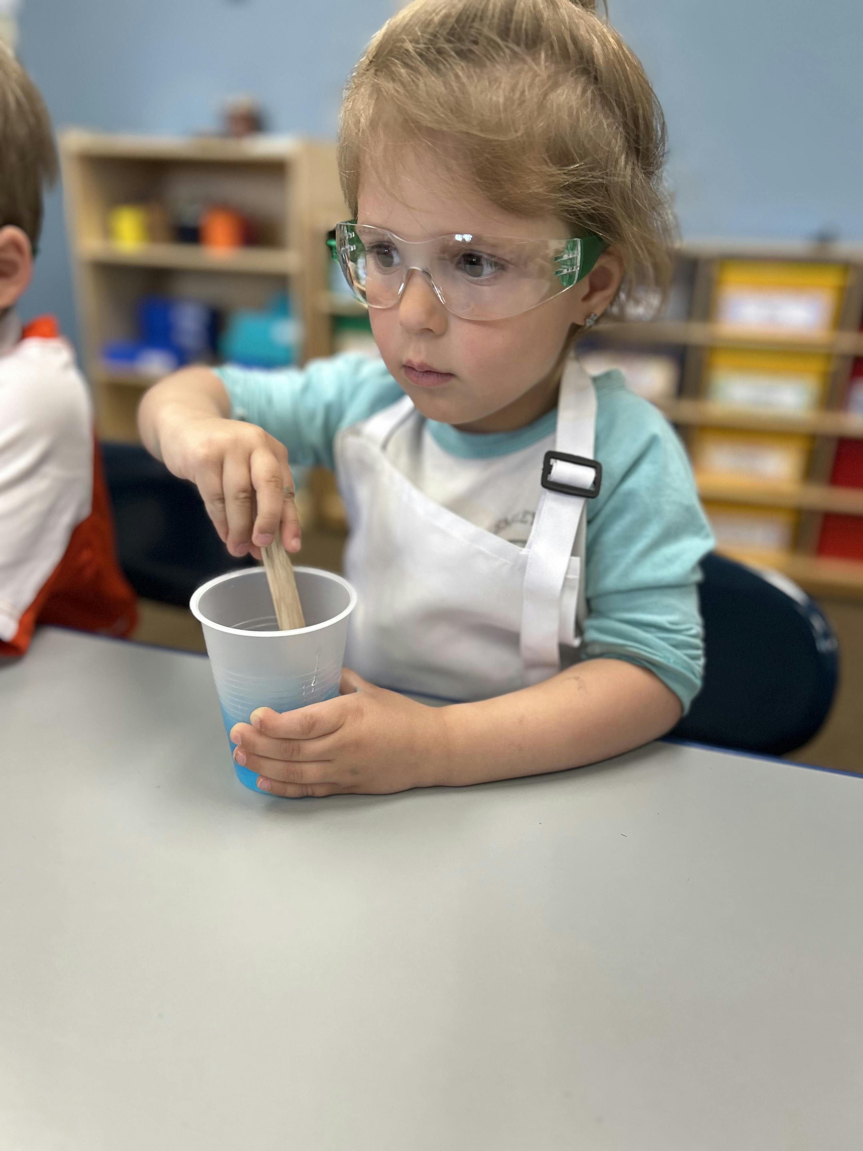 Child in safety glasses and apron stirring a cup