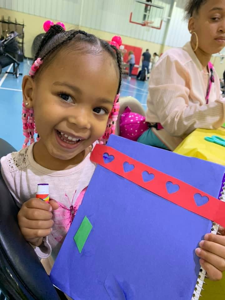 Child holding a glue stick and a blue notebook with a red heart-cutout strip