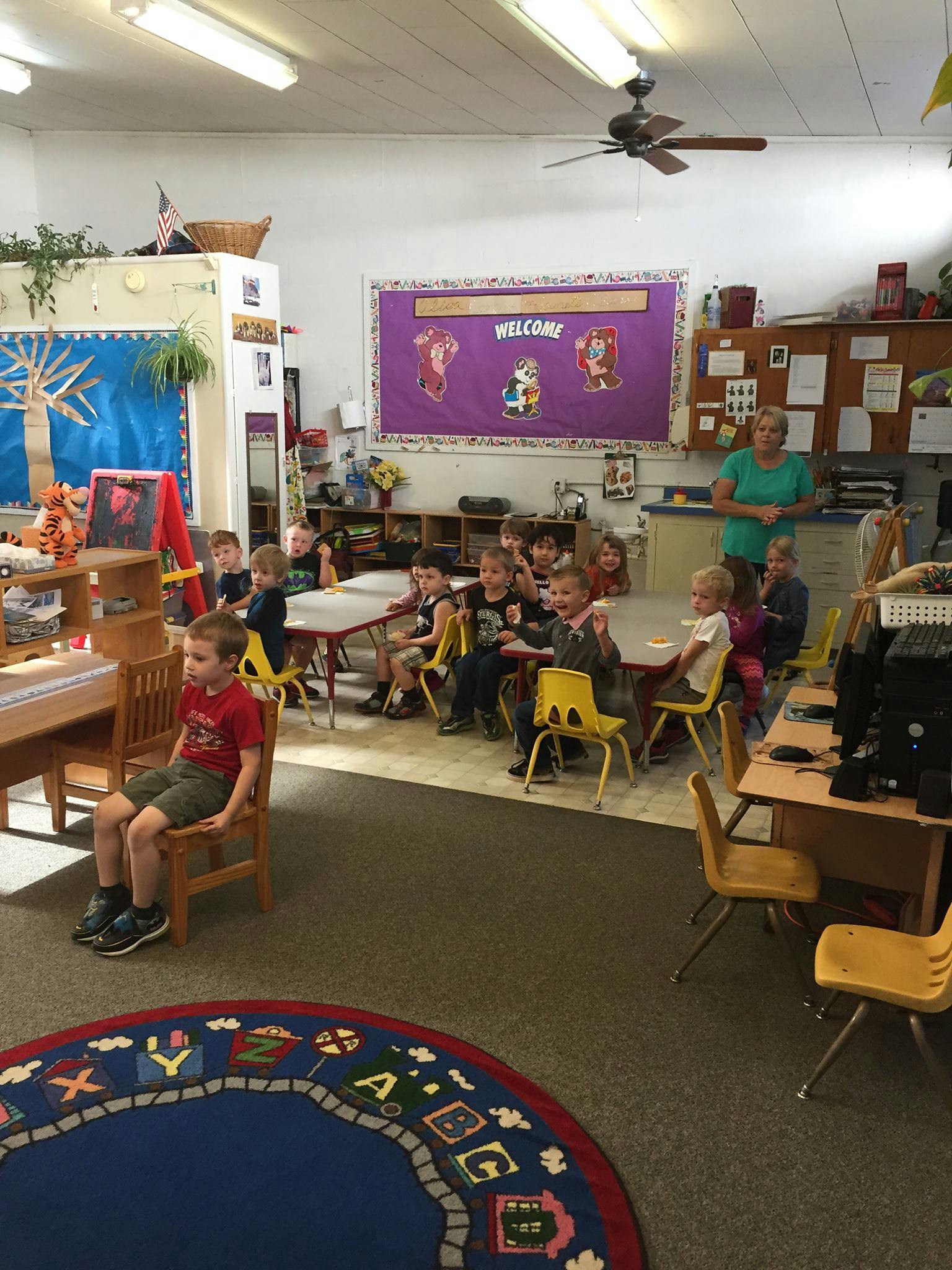 Children and an adult in a classroom with a "Welcome" sign