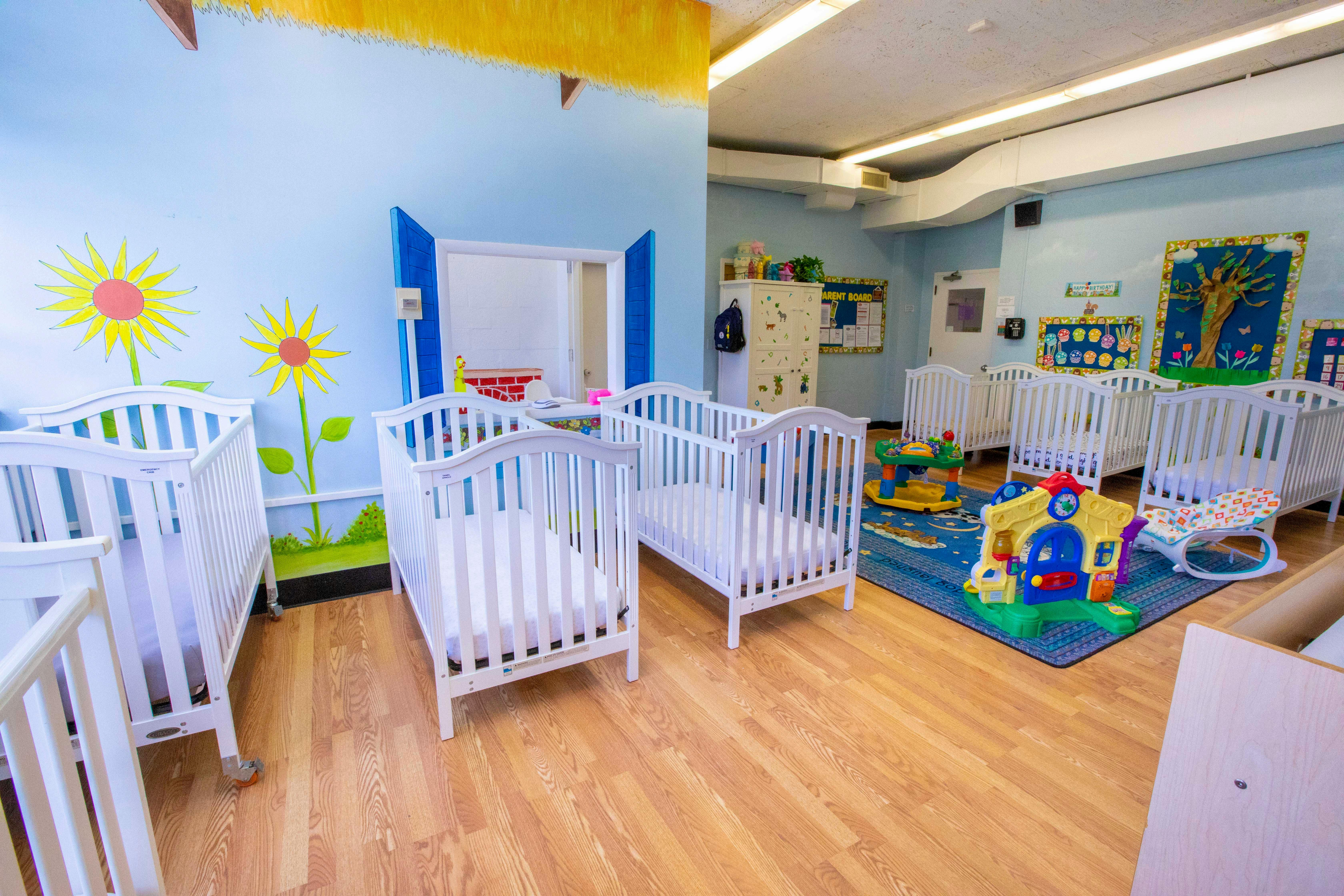 Multiple white cribs in a room with light blue walls and wooden floor