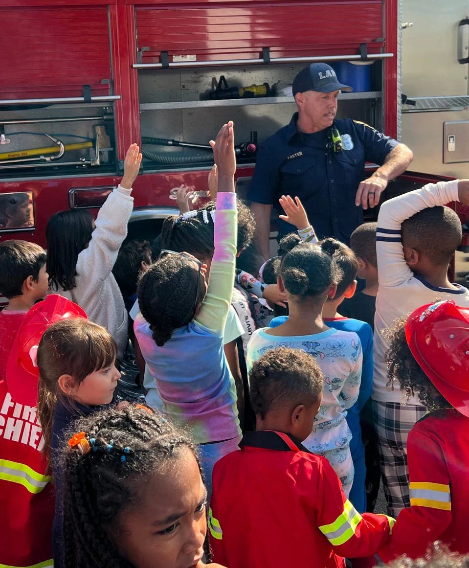 A person in uniform talking to a group of children with their hands raised