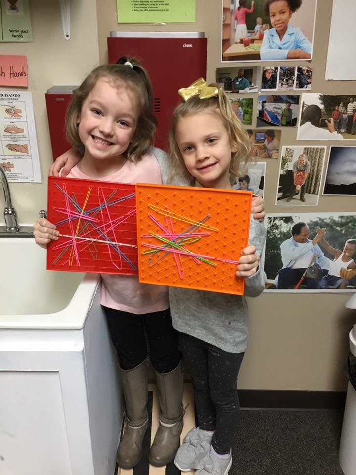 Two children holding up their colorful string art projects