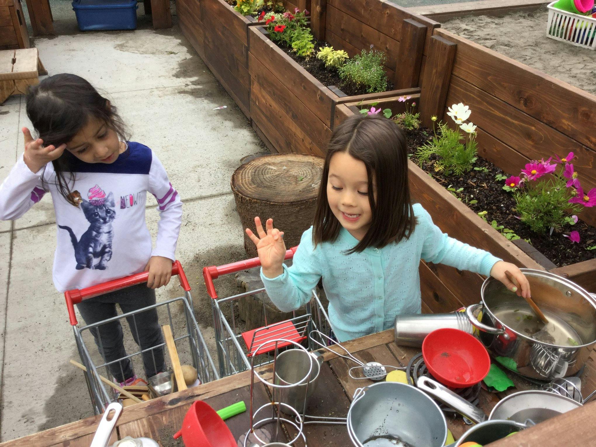 Two children playing with toy shopping carts and kitchen items outdoors