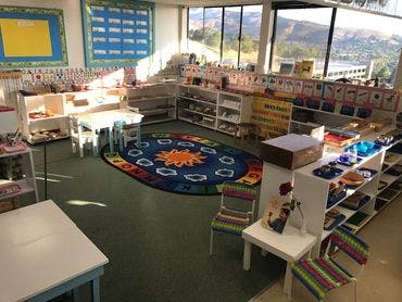 Classroom with tables, chairs, shelves, and a sun-patterned rug