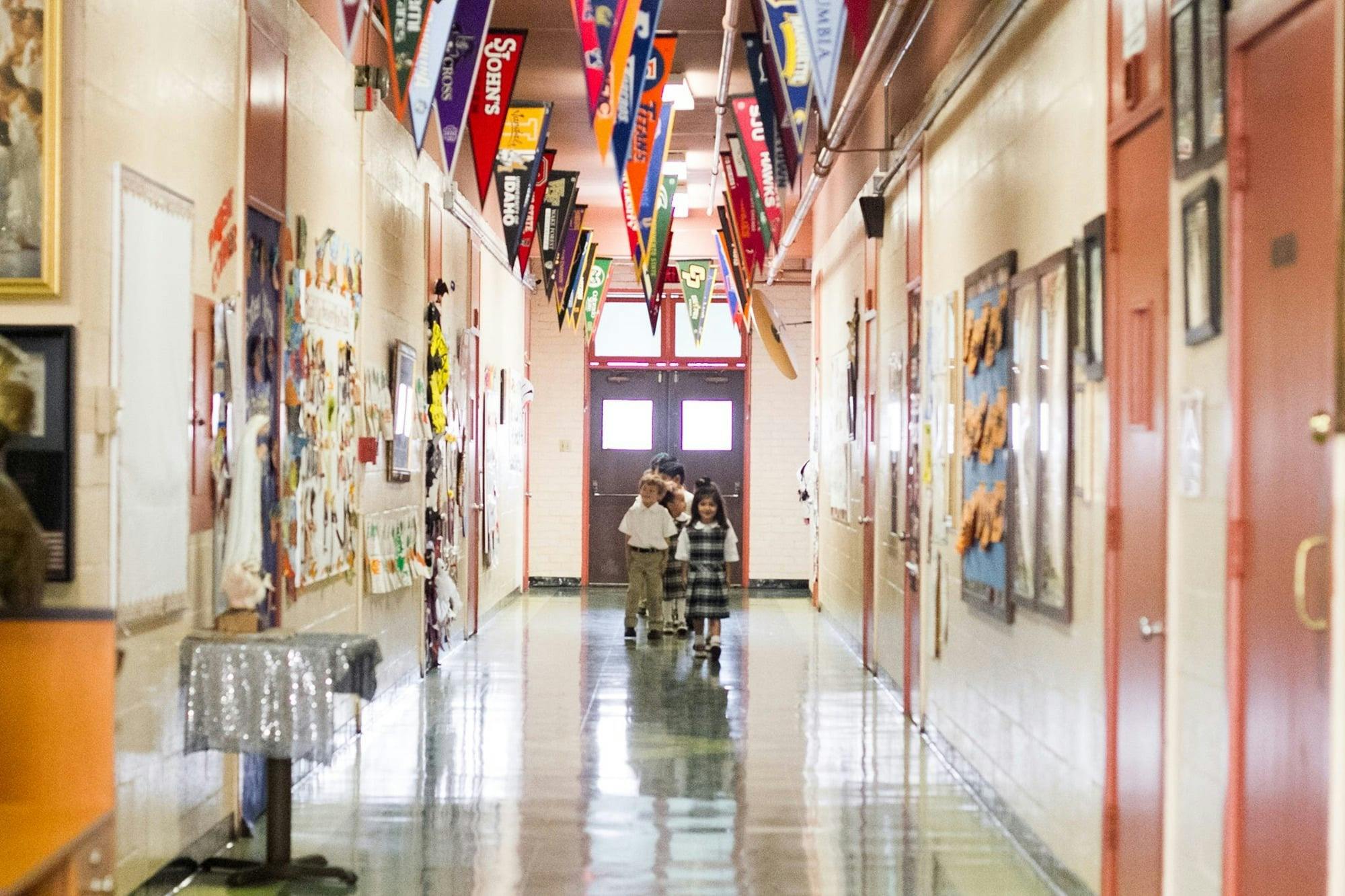 Children walking down a school hallway decorated with college pennants