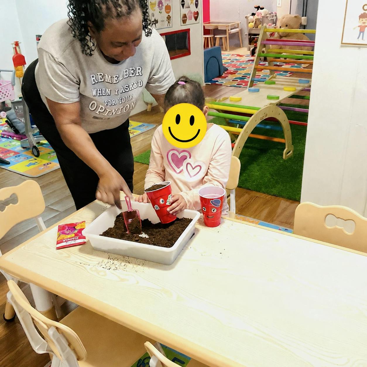 Adult and child scooping potting soil into plastic cups at a table