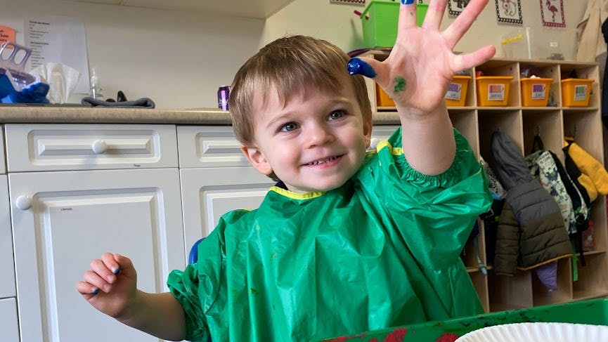 Child in green smock with paint on hand