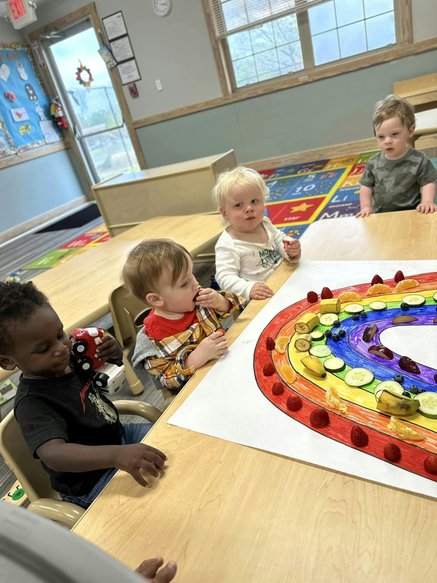 Three children at a table with a rainbow made of fruit