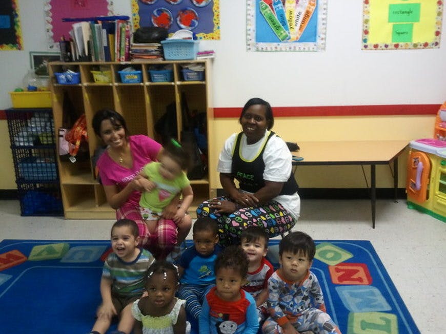 Two adults and several children sitting on a rug in a classroom