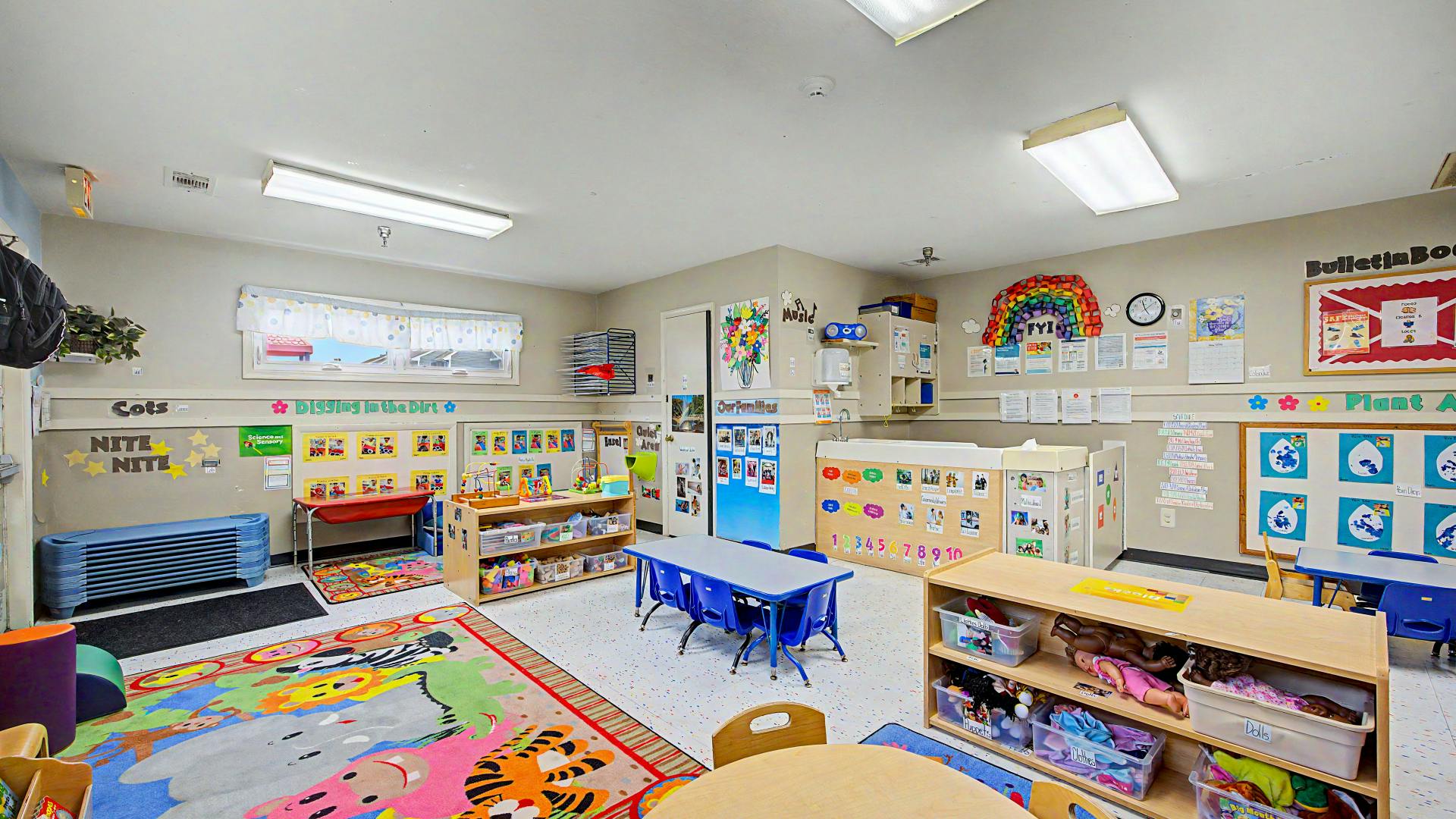 A classroom with activity areas, small tables and chairs, and a colorful rug