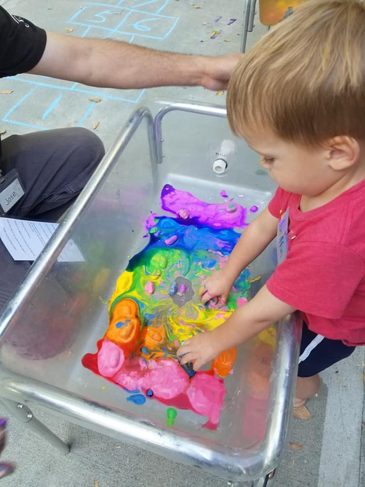Child playing with colorful paint in a metal tub