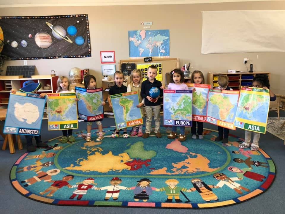 Children holding up maps of continents in a classroom