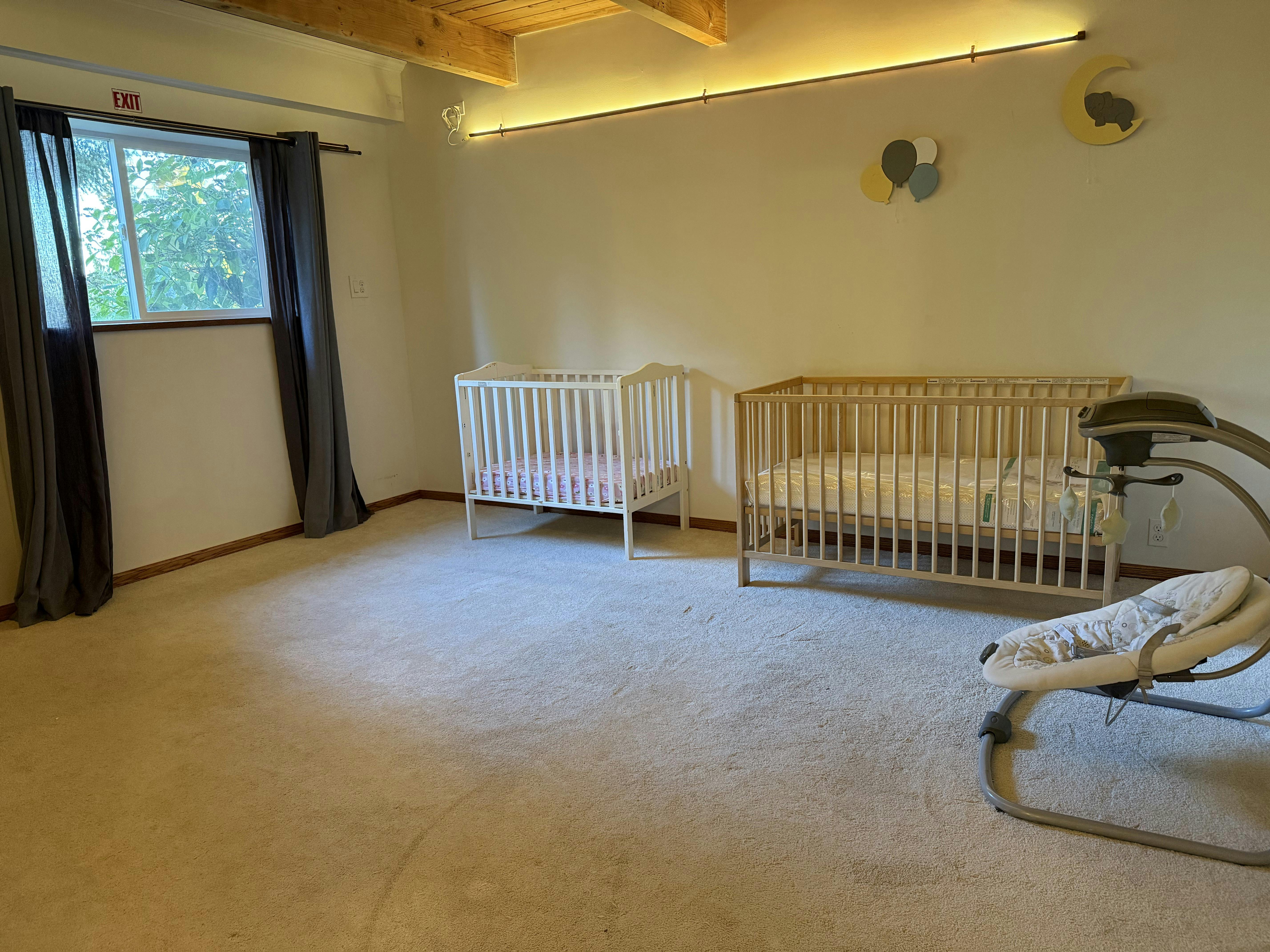 Two baby cribs and a baby swing in a room with a window