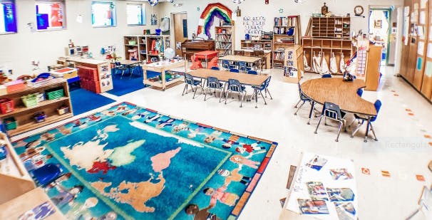 Empty classroom with tables, chairs, shelves, and a world map rug