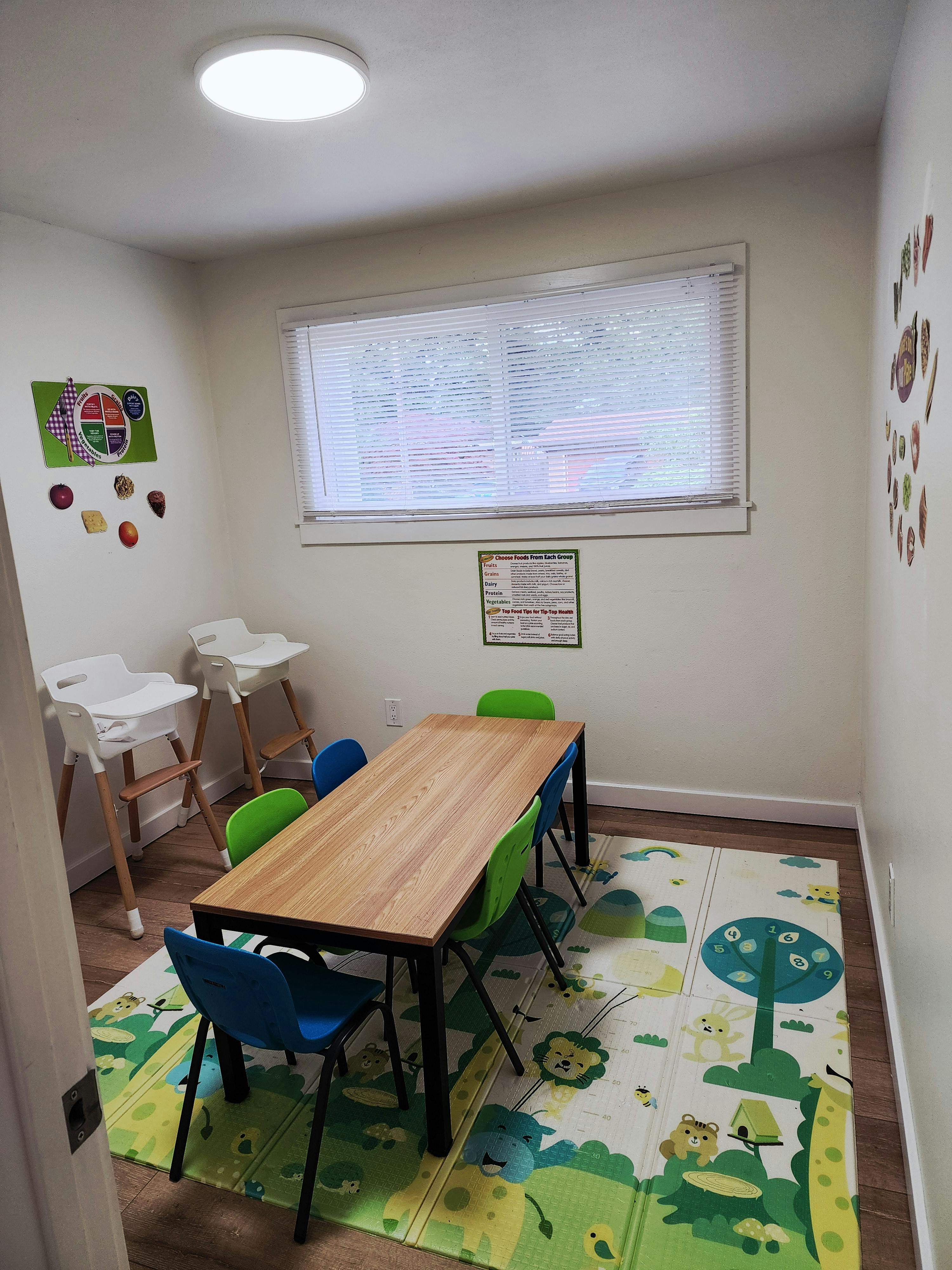 Childcare room with a wooden table, colorful chairs, and high chairs