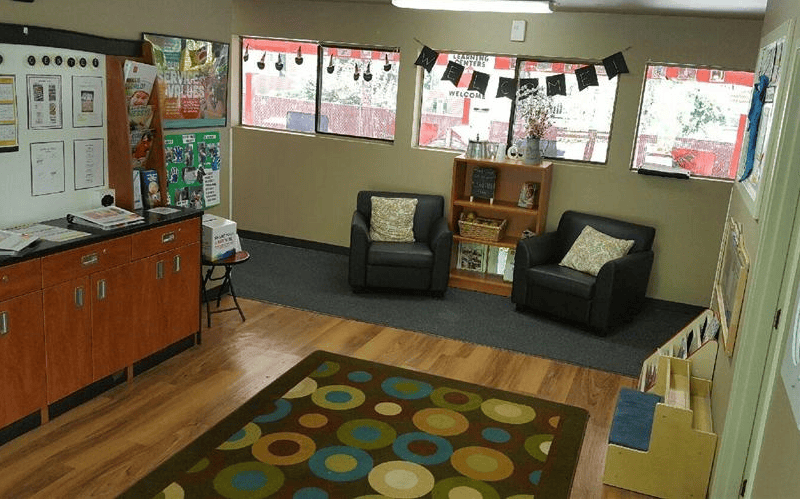 Lounge area with two chairs, a bookshelf, and a colorful rug on a wood floor