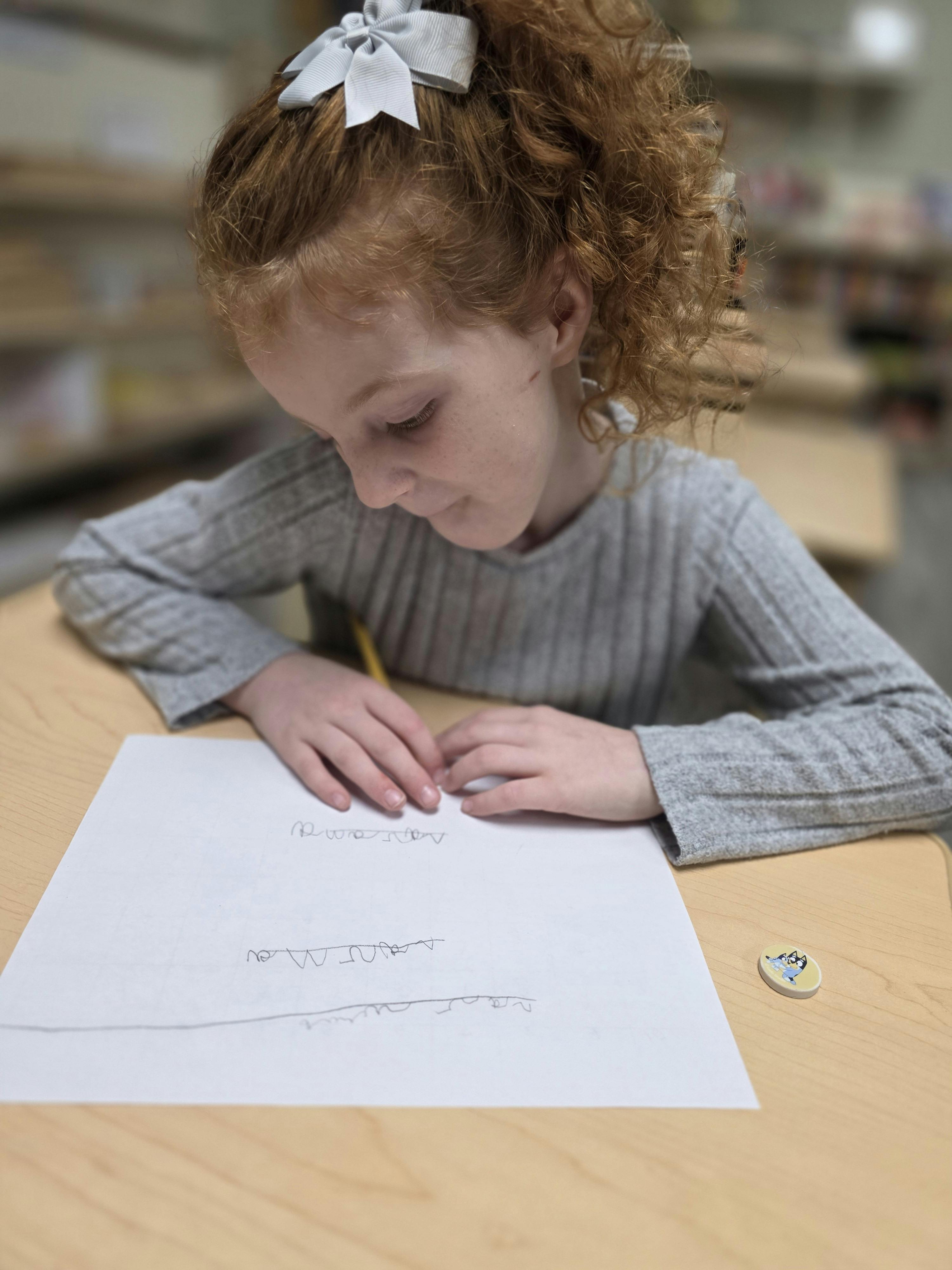 Child with curly hair writing on paper at a wooden desk