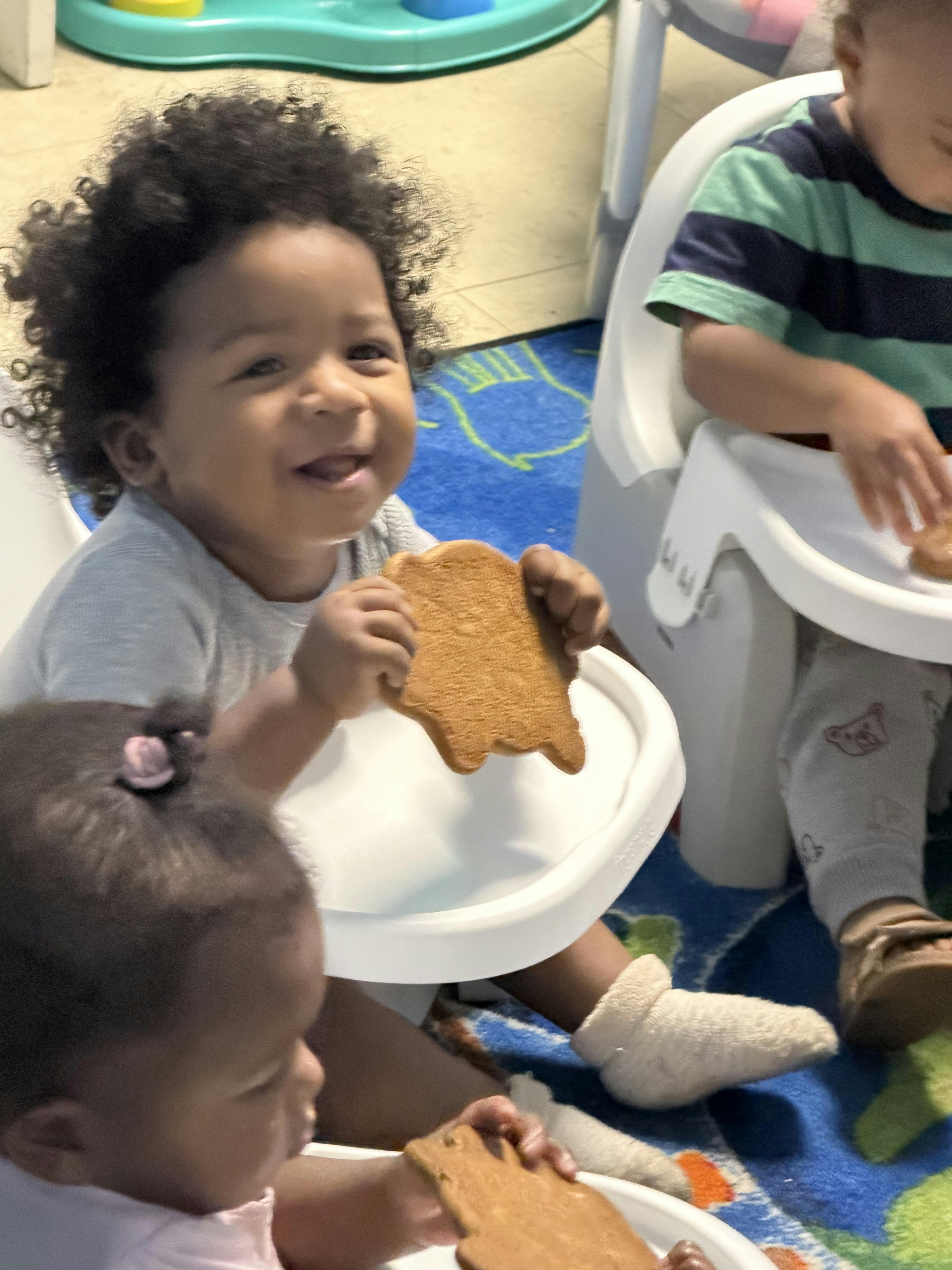 Child smiling while holding a cookie in a high chair