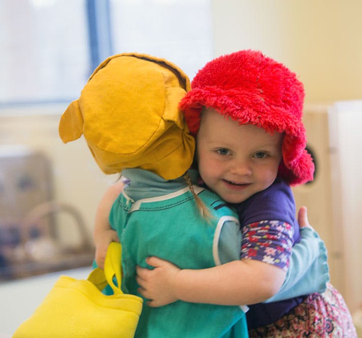 Child in red hat hugging another child