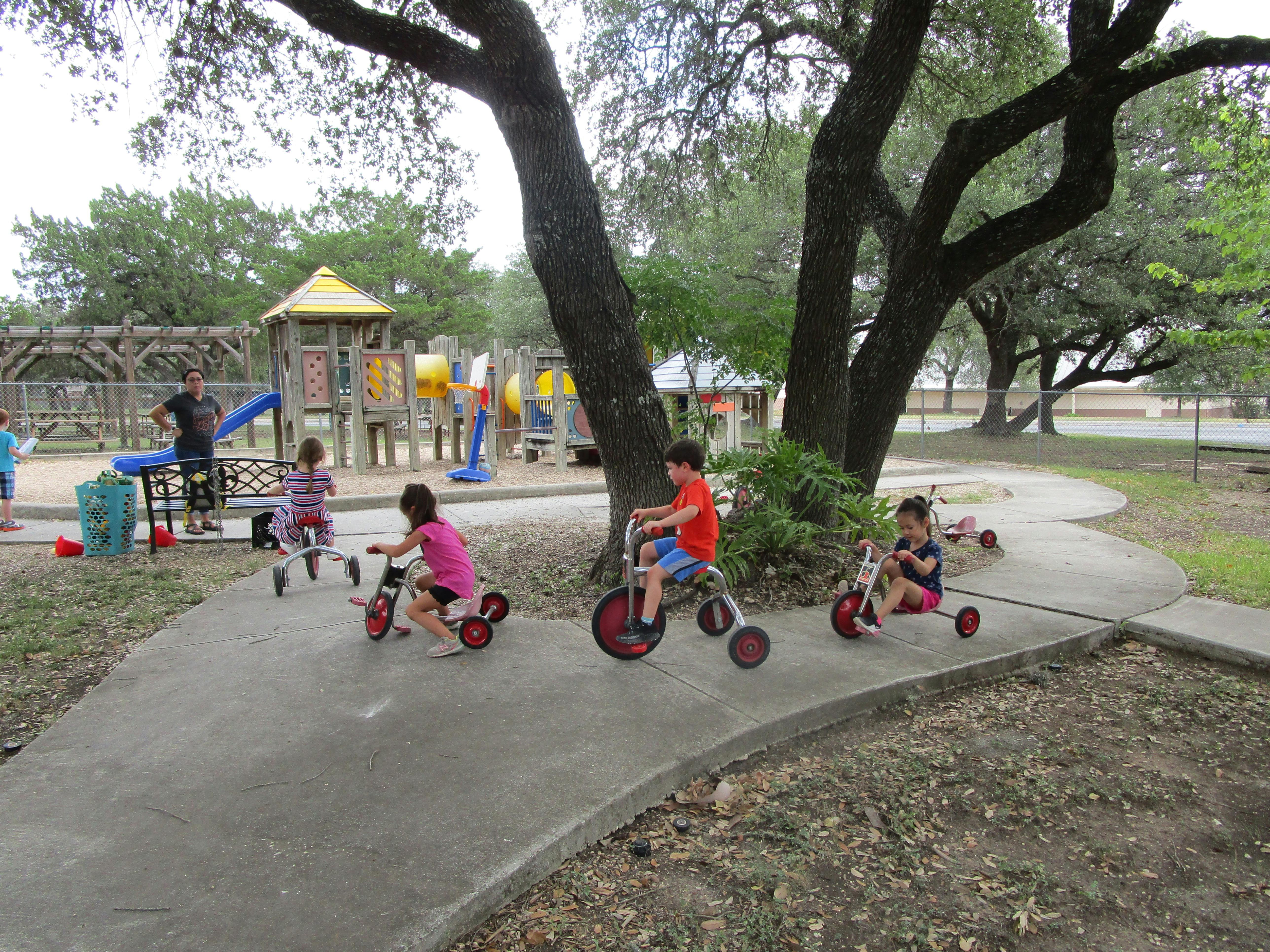 Children riding tricycles on a paved path in a park