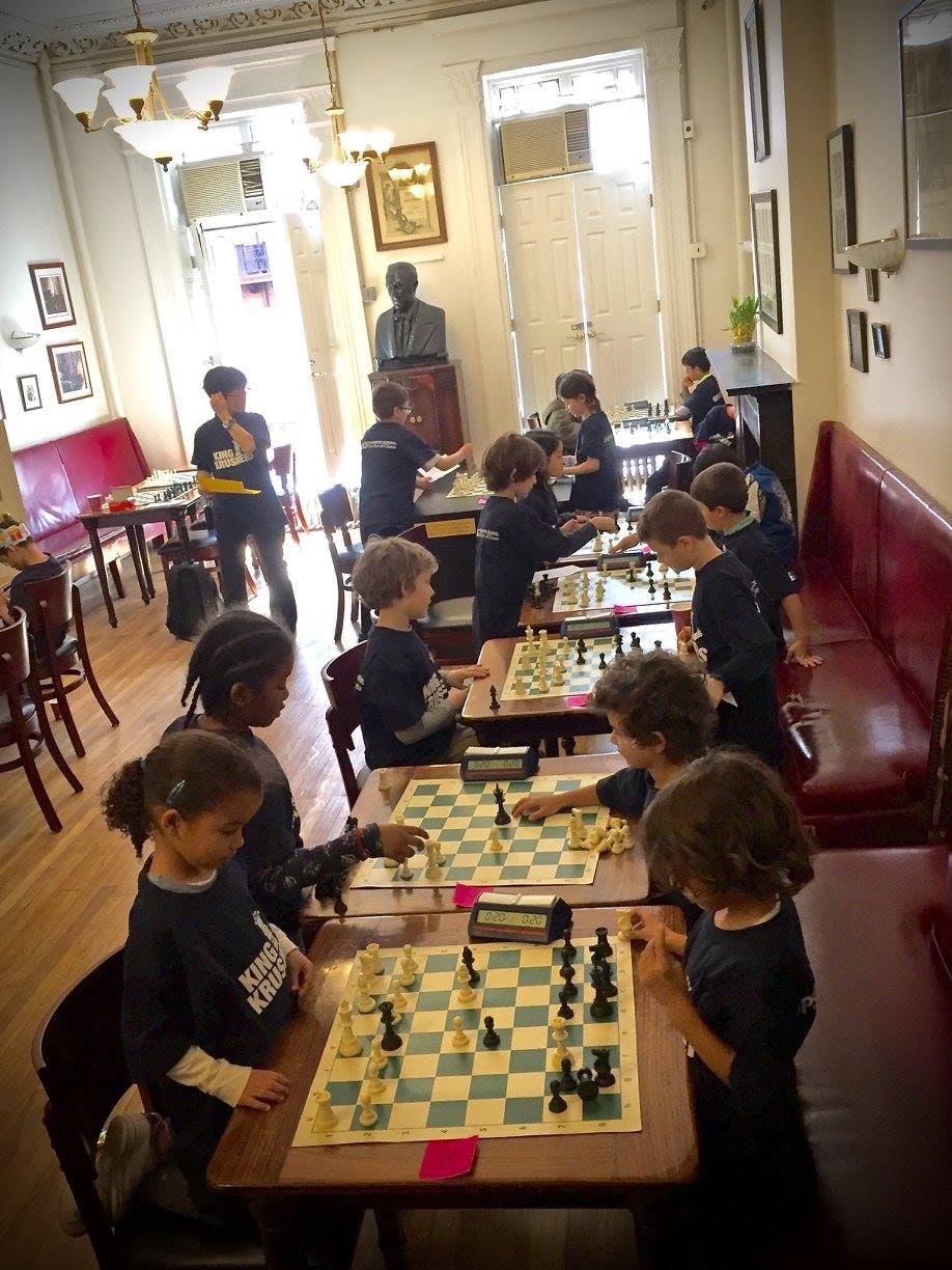 Children playing chess at tables in a room