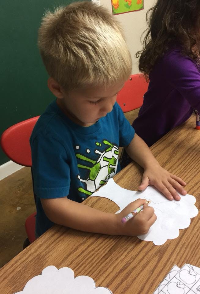 Child drawing on a paper cutout at a wooden table