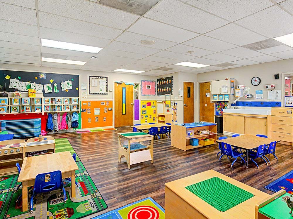 Empty classroom with small tables and chairs, shelves, and art on walls