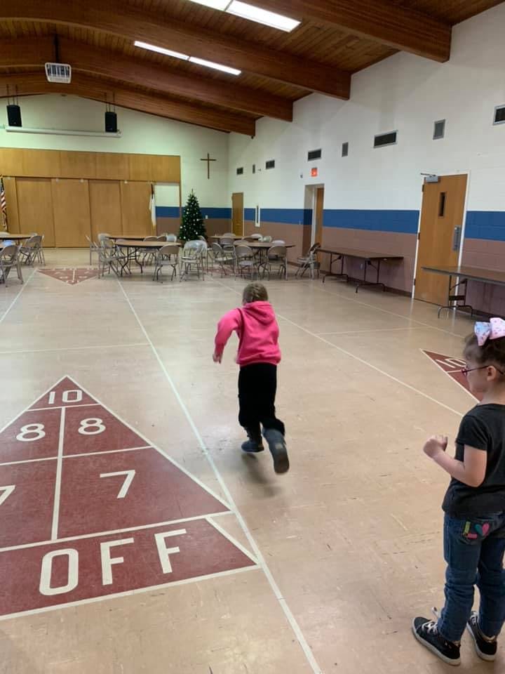 Child running on a shuffleboard court with another child watching