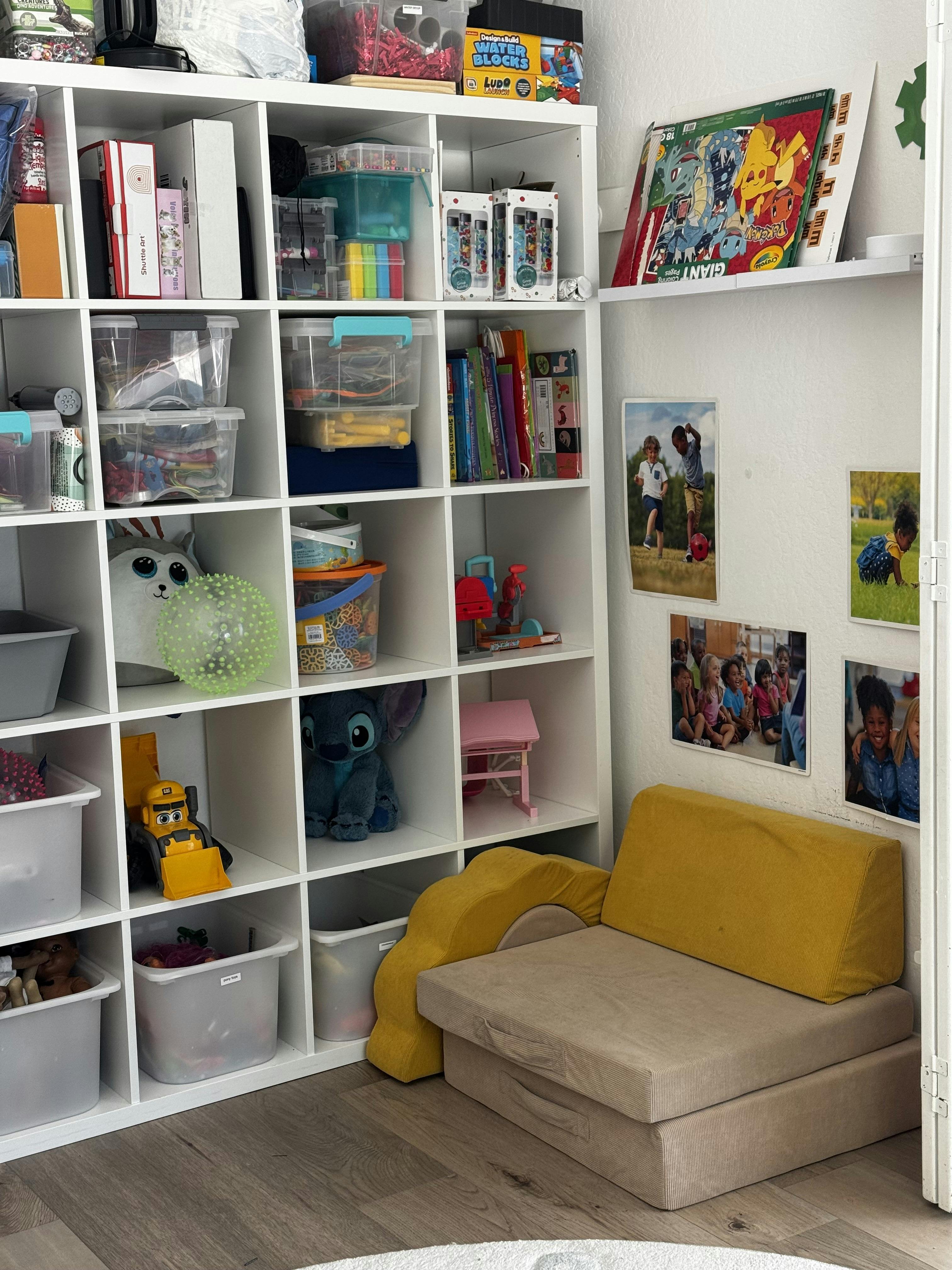A cube shelving unit filled with toys and books next to a yellow modular sofa