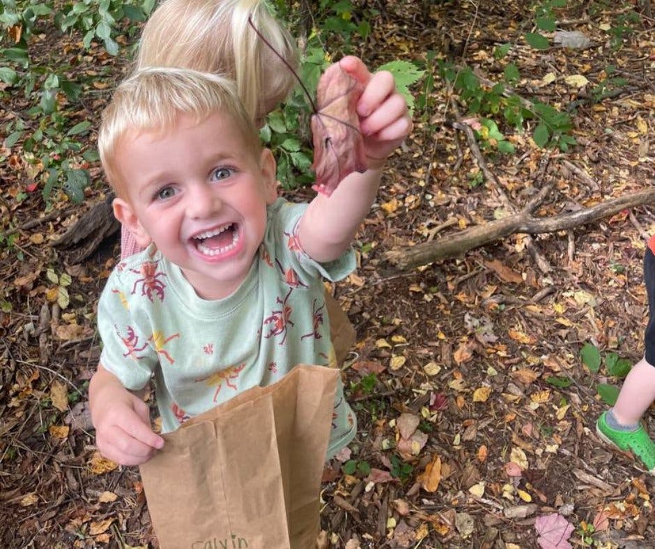 Child holding up a leaf while holding a paper bag